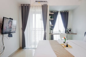 Ein Hotelzimmer mit Bett, Wandfernseher, Schreibtisch mit Stuhl und einem Fenster mit Vorhängen.