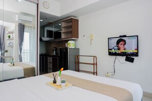 A hotel room with a bed, a TV, a desk, and a kitchenette. - Minimalist And Restful Studio Room At Apartment Grand Dhika City (Bekasi)