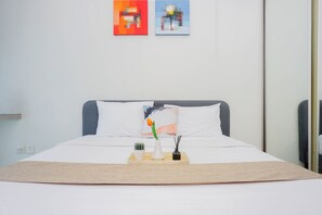 A neatly made bed with a white pillow, a small potted plant, and a tray with a vase and candle.