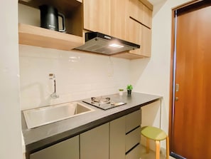 A kitchen with a sink, countertop, cabinets, a stove hood, and a small stool. - Practical Studio For 2 Pax At Grand Kamala Lagoon Apartment (Bekasi)