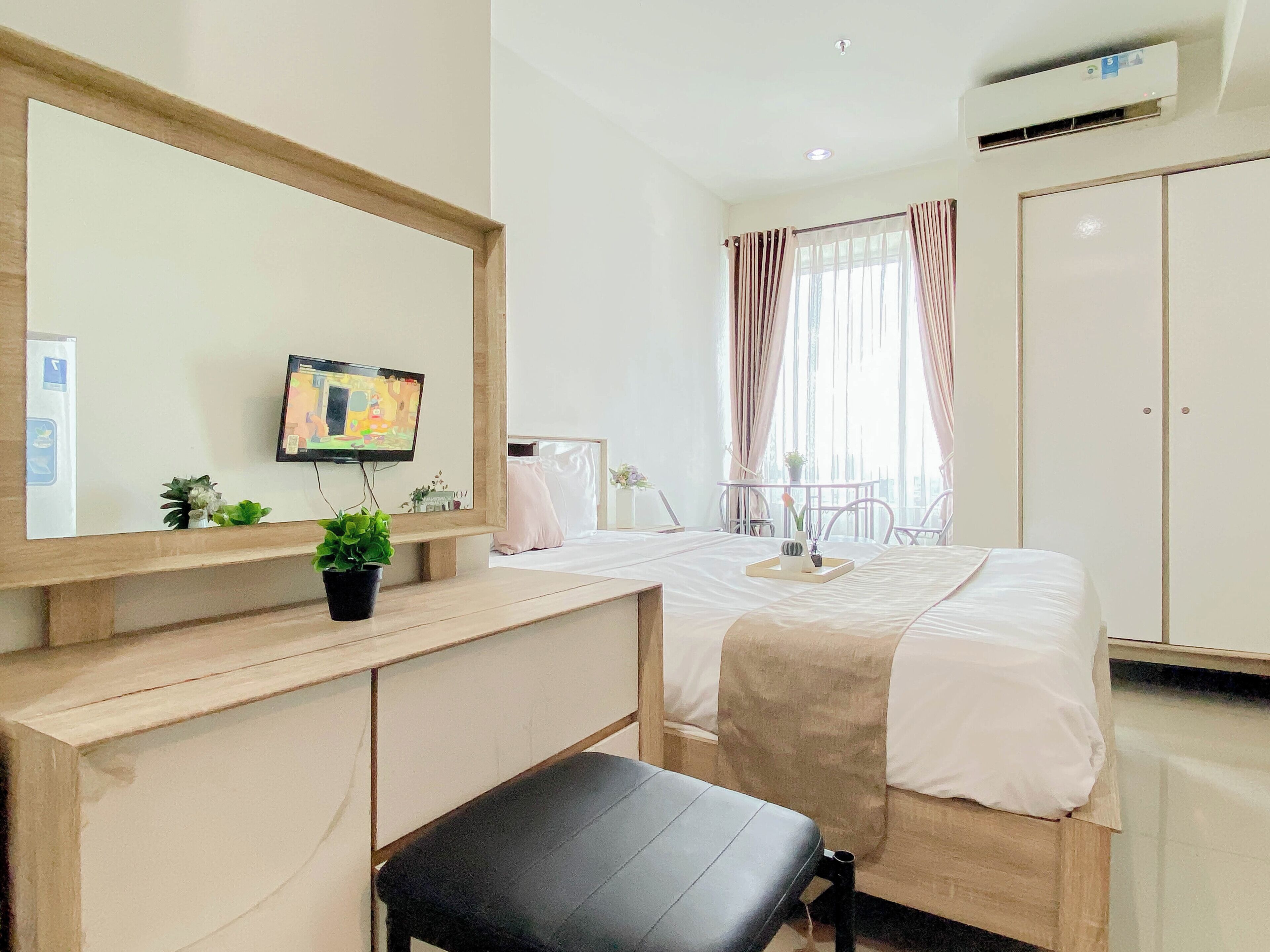 A hotel room with a bed, a desk with a computer, a chair, a TV, and a window with curtains.
