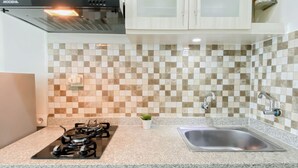 A kitchen with a gas stove, a stainless steel sink, and a checkered backsplash. - Practical And Restful Studio Room At Apartment Grand Kamala Lagoon (Bekasi)