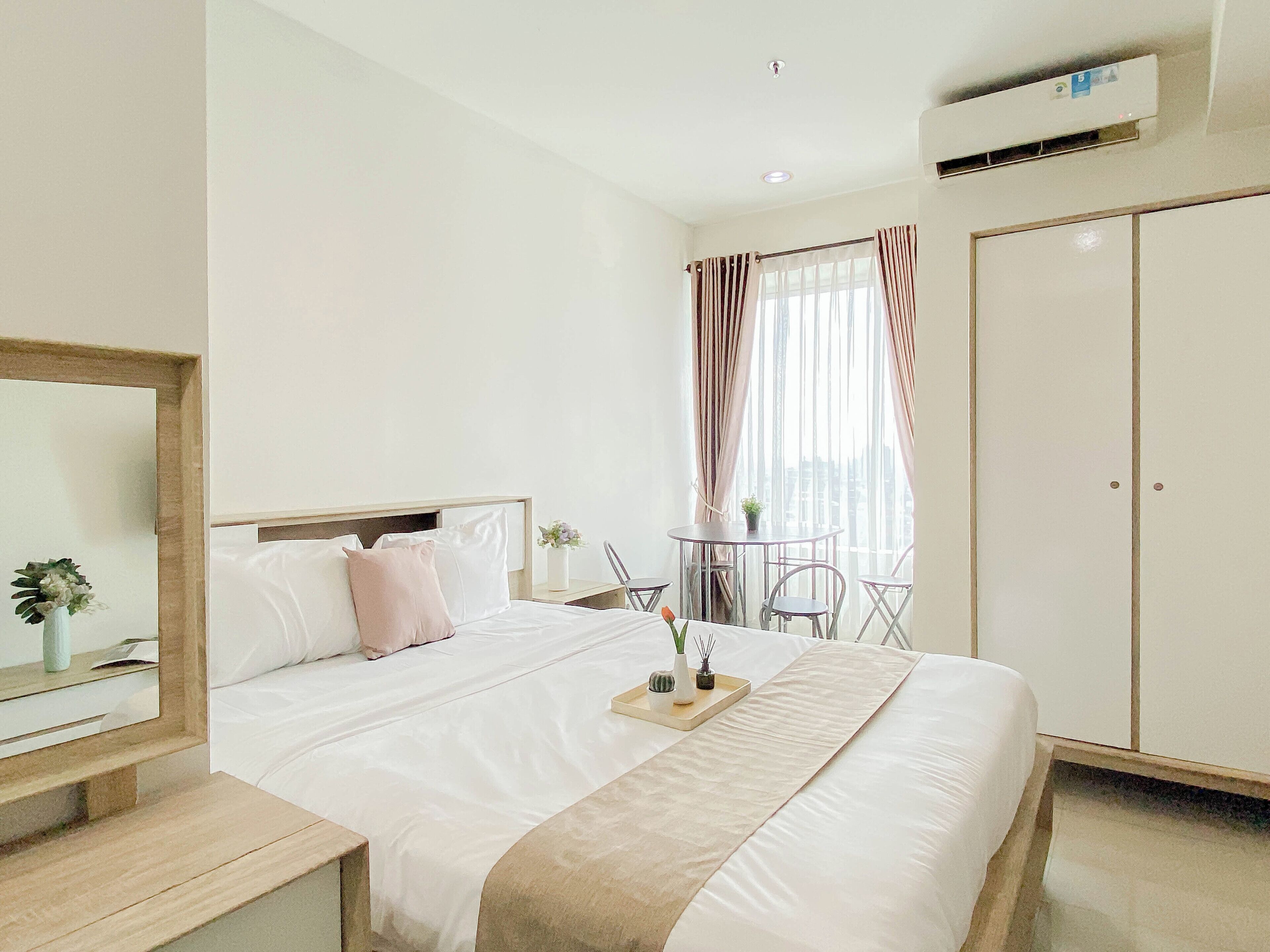 Een hotelkamer met een bed, nachtkastje, spiegel, kledingkast en een klein balkon met een tafel en stoelen.