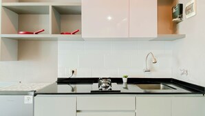 A modern kitchen with white cabinets, a black countertop, a built-in oven, and a stainless steel faucet. - Restful Stay In Studio Room At Apartment Grand Kamala Lagoon (Bekasi)
