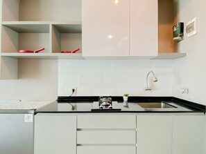 A modern kitchen with white cabinets, a black countertop, a built-in oven, and a stainless steel faucet. - Restful Stay In Studio Room At Apartment Grand Kamala Lagoon (Bekasi)
