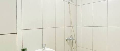 Un baño con azulejos blancos, un lavamanos, una ducha y una pequeña planta en maceta.
