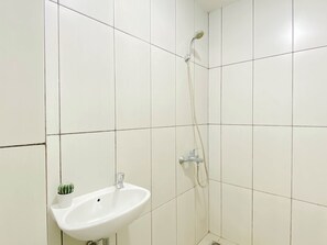 A bathroom with white tiles, a sink, a shower, and a small potted plant. - Restful Stay In Studio Room At Apartment Grand Kamala Lagoon (Bekasi)