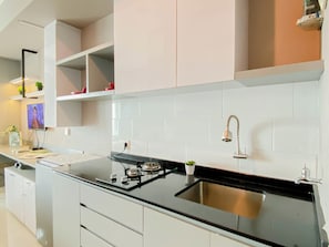 A modern kitchen with white cabinets, a black countertop, a stainless steel sink, and a built-in stove. - Restful Stay In Studio Room At Apartment Grand Kamala Lagoon (Bekasi)