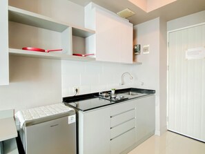 A modern kitchen with white cabinetry, a black countertop, and a compact refrigerator. - Restful Stay In Studio Room At Apartment Grand Kamala Lagoon (Bekasi)