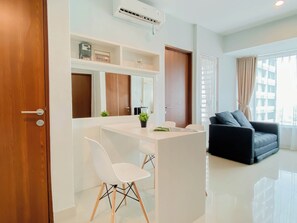A modern living room with a black sofa, a white dining area, and a large window with curtains. - Classic 1Br With Extra Room At Apartment Grand Kamala Lagoon (Bekasi)