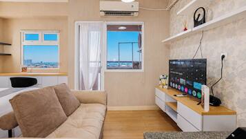 A modern living room with a sofa, a TV, a desk, and a window with a city view.