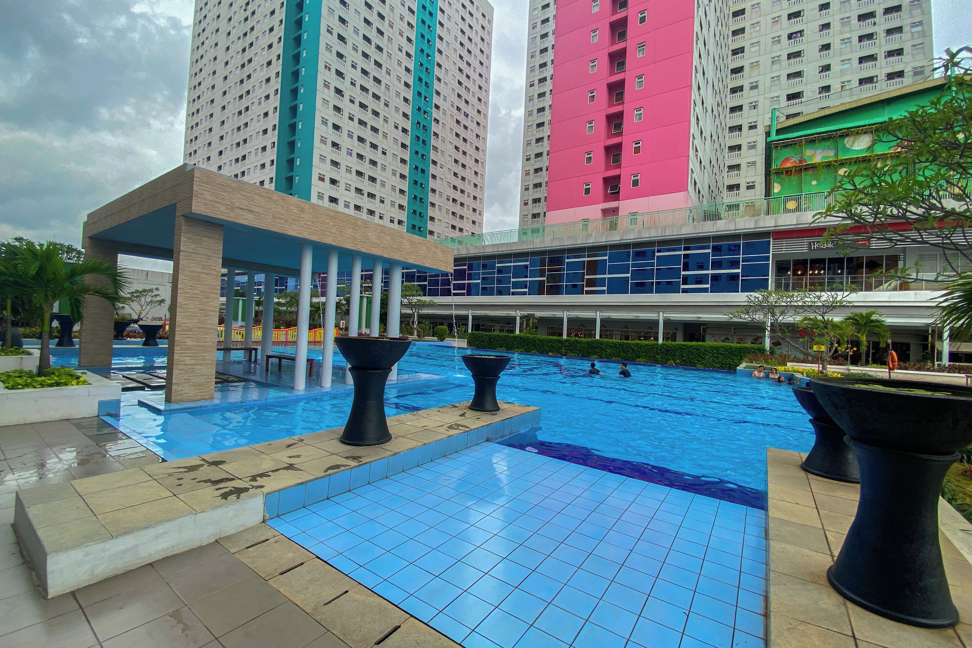 A swimming pool area with tiled flooring, black planters, and a covered seating area.