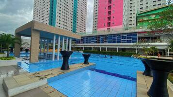 A swimming pool area with tiled flooring, black planters, and a covered seating area.