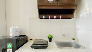 A compact kitchen with a countertop, a rice cooker, a scale, a sink, and a cabinet with a low voltage warning sign. - Practical Studio At Gunung Putri Square Apartment (Gunung Putri)