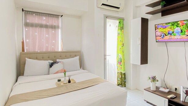 A bedroom with a bed, a TV, an air conditioner, and a window with curtains. - Practical Studio At Gunung Putri Square Apartment (Gunung Putri)