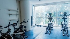Un gimnasio con bicicletas estáticas, un estante en la pared y ventanas amplias.