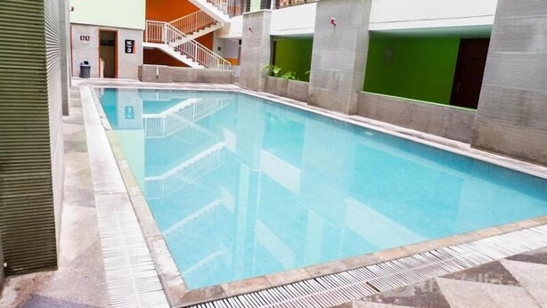 Una piscina interior con solárium de baldosas, una escalera y una pared verde.