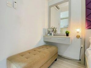 Quarto com cama, mesa de cabeceira com abajur, espelho e um pequeno banco.