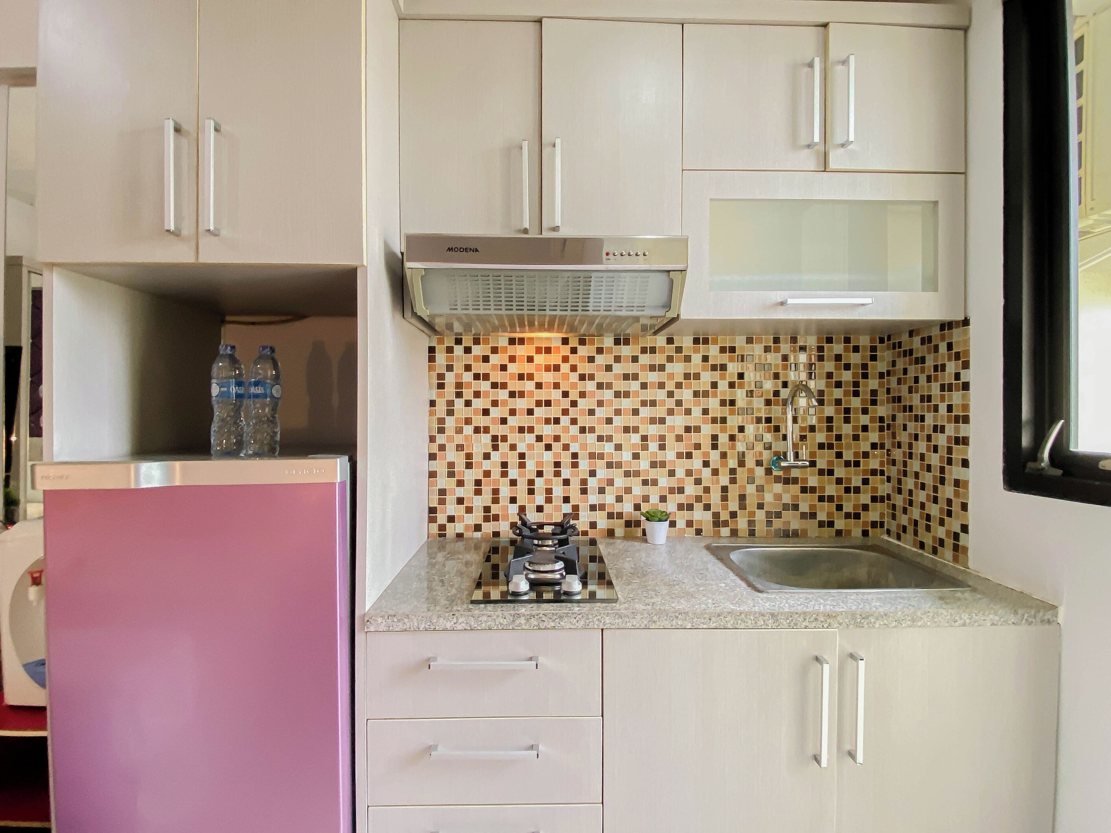 Una cucina con mobili bianchi, un frigorifero rosa, uno schienale piastrellato, un lavello in acciaio inossidabile e una cucina a gas.