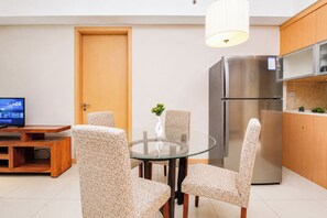A modern kitchen with a stainless steel refrigerator, a dining table with four chairs, and a television on a wooden stand. - Gorgeous And Cozy 2Br Apartment Kemang Village (Jakarta)