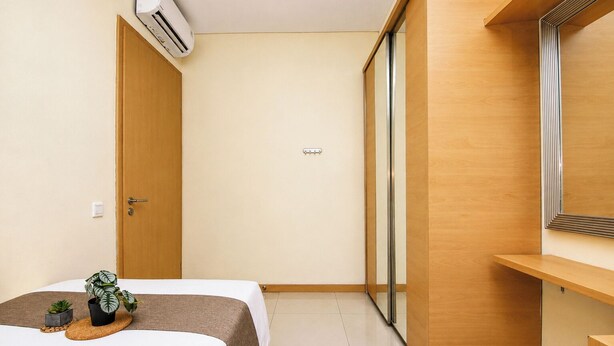 Quarto de hotel com uma cama, uma mesinha com uma planta, um espelho e uma porta de correr.
