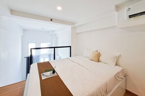 A hotel room with a bed, a small table with a plant, a window, and an air conditioning unit. - Serene Loft Studio At Kingland Avenue Apartment (South Tangerang)