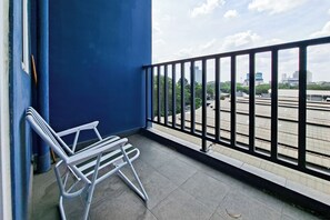 A balcony with a white metal chair, a blue wall, and a view of a cityscape. - Serene Loft Studio At Kingland Avenue Apartment (South Tangerang)