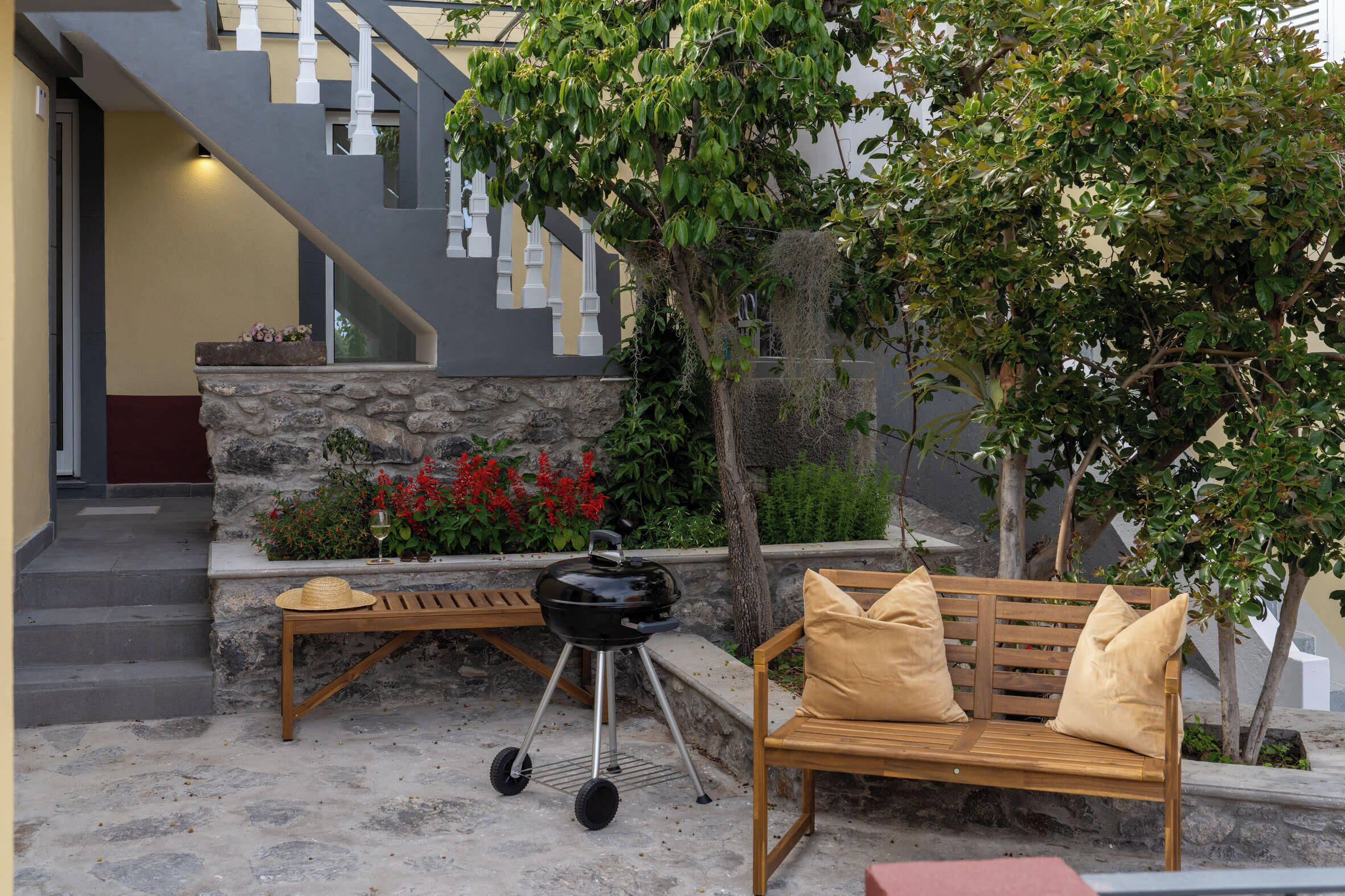 Un patio con un banco de piedra, un banco de madera, una parrilla y una escalera que lleva a un nivel superior.