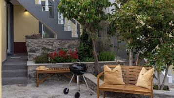 Un patio con un banco de piedra, un banco de madera, una parrilla y una escalera que lleva a un nivel superior.