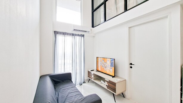 A modern living room with a sofa, TV, and a white door. - Convenient 3Br Loft With Modern Style At Kingland Avenue Apartment (South Tangerang)