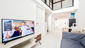 A modern living room with a large flat-screen TV, a grey sofa, and a white entertainment unit. - Convenient 3Br Loft With Modern Style At Kingland Avenue Apartment (South Tangerang)
