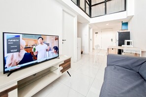 A modern living room with a large flat-screen TV, a grey sofa, and a white entertainment unit. - Convenient 3Br Loft With Modern Style At Kingland Avenue Apartment (South Tangerang)