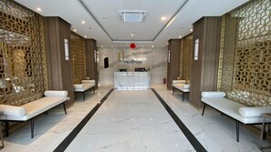 A hotel lobby with a reception desk, two seating areas, and a marble floor. - Convenient 3Br Loft With Modern Style At Kingland Avenue Apartment (South Tangerang)