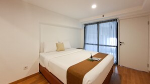 A hotel room with a single bed, a wooden floor, a white wall, and a window with curtains. - Convenient 3Br Loft With Modern Style At Kingland Avenue Apartment (South Tangerang)
