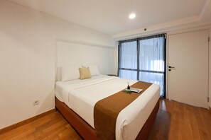 A hotel room with a single bed, a wooden floor, a white wall, and a window with curtains. - Convenient 3Br Loft With Modern Style At Kingland Avenue Apartment (South Tangerang)