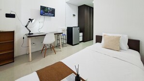 A hotel room with a bed, desk, chair, TV, and a refrigerator. - Comfy And Nice Studio (No Kitchen) At Apartment Kubikahomy (Pagedangan)