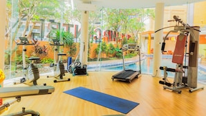 A gym with exercise equipment, a blue mat, and a view of a swimming pool and greenery outside. - Comfy And Nice Studio (No Kitchen) At Apartment Kubikahomy (Pagedangan)