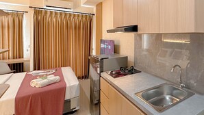 Quarto de hotel compacto com cozinha compacta, cama com colcha vermelha e área de chuveiro.