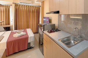 Habitació d'hotel compacta amb cuineta, un llit amb col·cha vermella i zona de dutxa.
