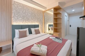 A hotel room with a bed, a bedside table, a mirror, a wardrobe, and a television. - Comfy Studio At Kyo Society Apartment (Surabaya)
