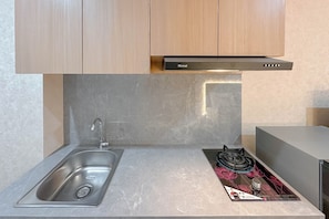 A kitchen with a stainless steel sink, a gas stove, and a Rinnai range hood. - Comfy Studio At Kyo Society Apartment (Surabaya)