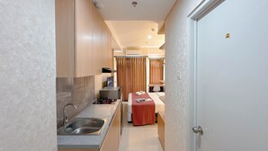 Een compacte hotelkamer met kitchenette, een bed met een rode deken en een deur met een gouden slot.