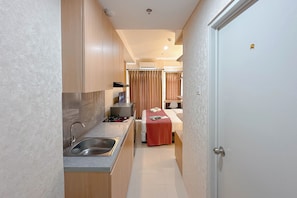 A compact hotel room with a kitchenette, a bed with a red blanket, and a door with a gold lock. - Comfy Studio At Kyo Society Apartment (Surabaya)
