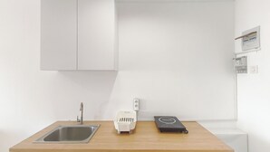A kitchen with a stainless steel sink, a white trash bin, and a black appliance on a wooden countertop. - Zen Style Studio At Kyo Society Apartment (Surabaya)