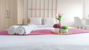 Habitación de hotel con cama, almohadas, una toalla enrollada, una bandeja con plantas en macetas y una silla.