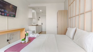Ein Hotelzimmer mit Bett, Fernseher, Schreibtisch mit Computer, kleiner Küchenzeile und Holzschrank.