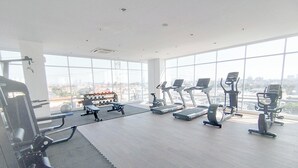 Een fitnessruimte met diverse trainingsapparaten, grote ramen en uitzicht op de stad.