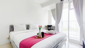 Een hotelkamer met een bed, nachtkastje, stoel, raam met gordijnen en uitzicht op het omliggende landschap.