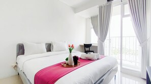 Ein Hotelzimmer mit Bett, Nachttisch, Stuhl, einem Fenster mit Vorhängen und Blick ins Freie.