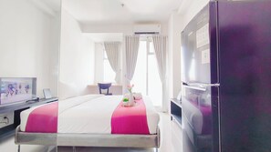 Ein Hotelzimmer mit einem Bett, einem Schreibtisch mit Computer, einem Fernseher, einem Kühlschrank und einem Fenster mit Vorhängen.